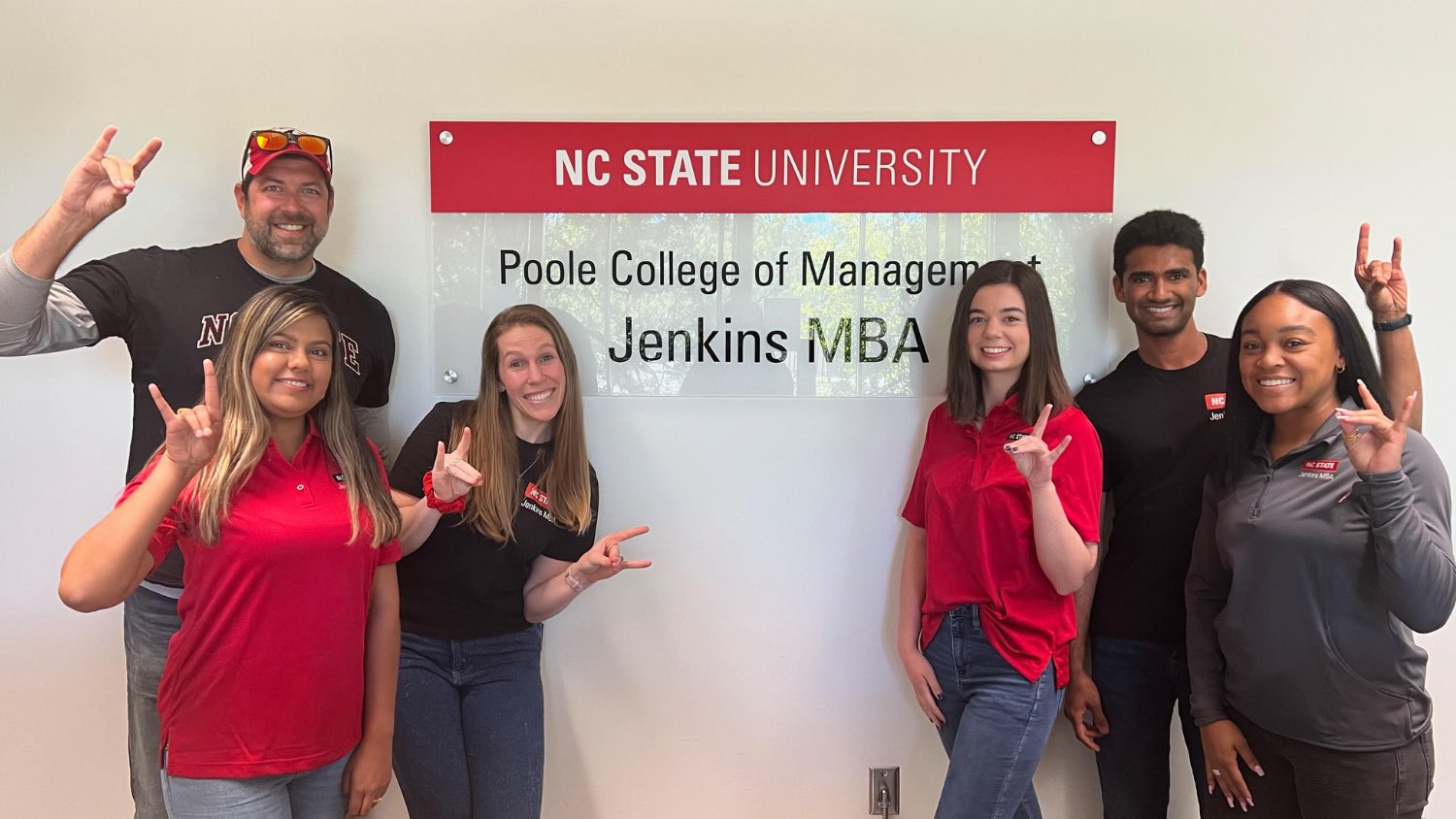 Six MBA students posing the wolfpack sign in front of the MBA sign.