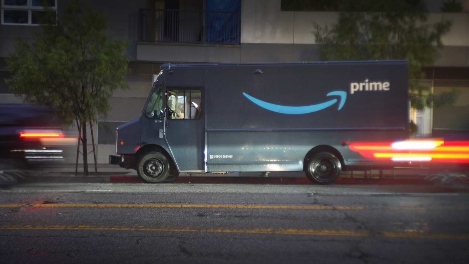 A blue Amazon truck drives on a city street.