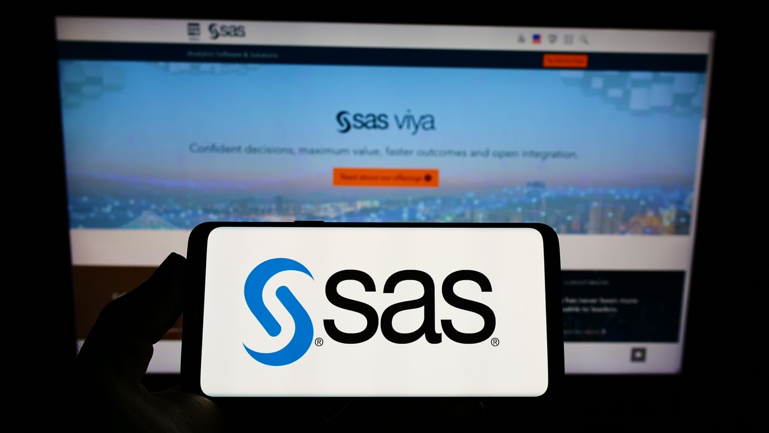 Person holding smartphone with logo of US analytics software company SAS Institute Inc. on screen in front of website.