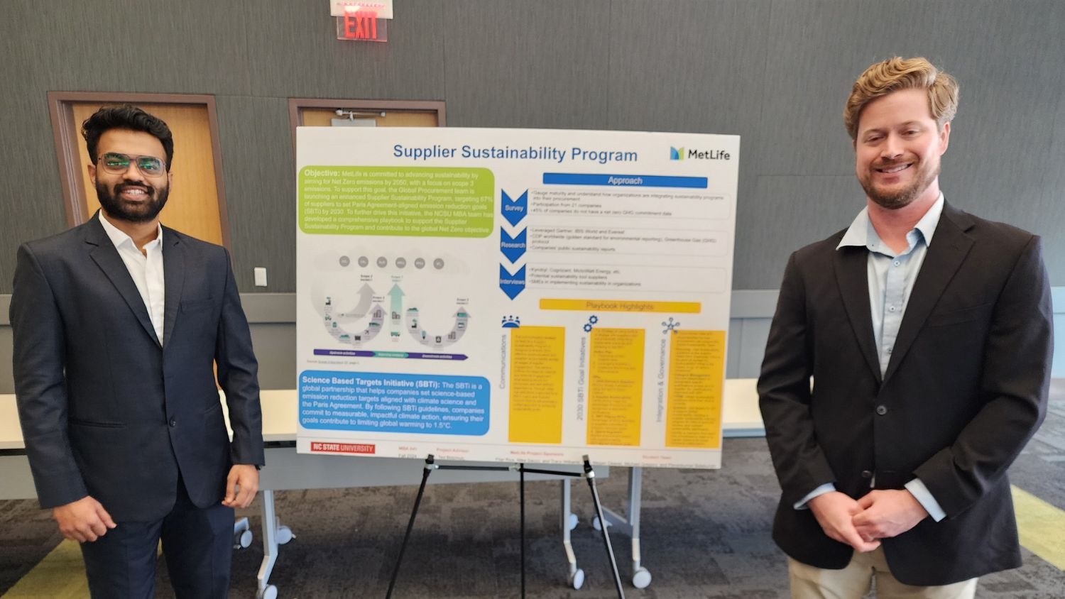 Two students smile in front of presentation board